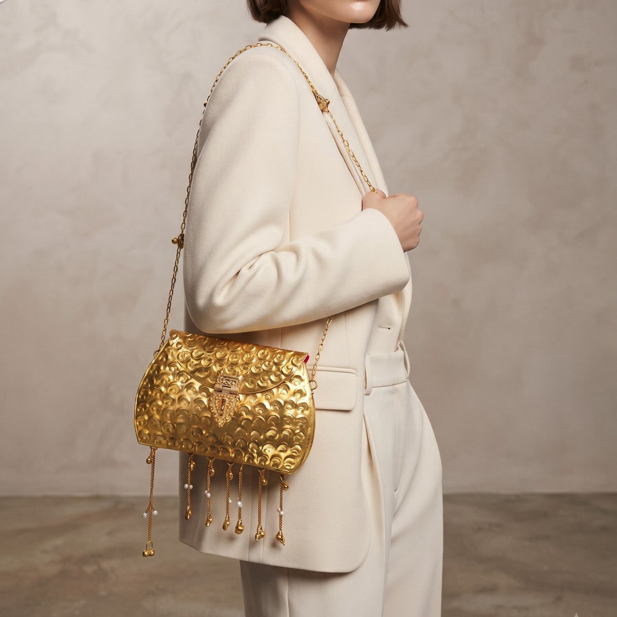 The Pearl Rain Handbag — hammered scale-textured gold-tone flap bag with a chain-and-pearl fringe, worn on the shoulder